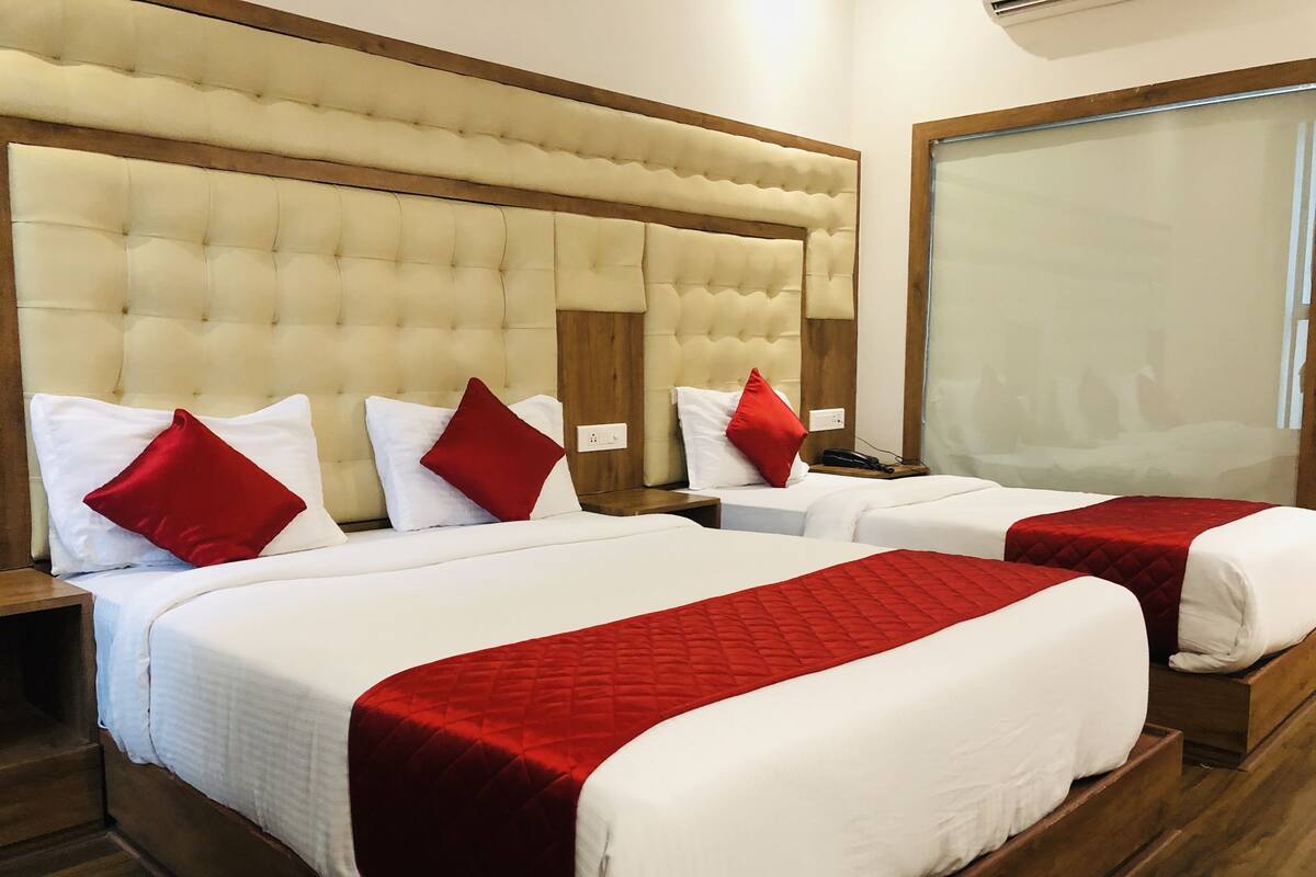 A hotel room with two beds, each with white bedding and red pillows. The room has a wooden headboard and a large window.