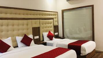A hotel room with two beds, each with red and white bedding, a large window, and an air conditioning unit on the wall.