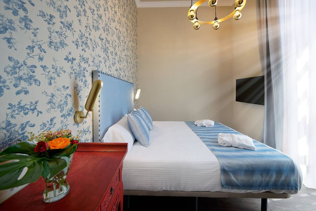 Habitación de hotel con una cama, una mesita de noche con un florero y un televisor montado en la pared.