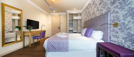 A hotel room with a bed, a desk with a chair, a television, a mirror, and a wardrobe.
