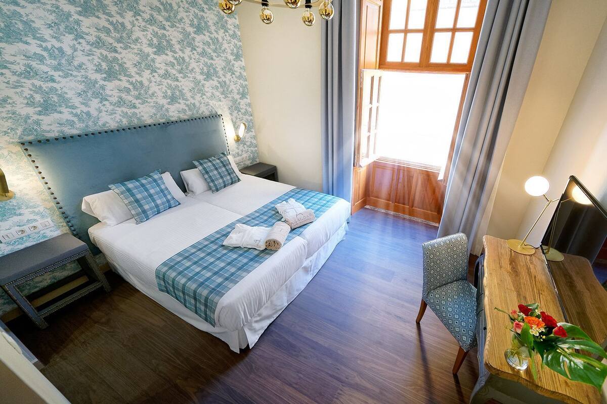 Una habitación de hotel con una cama grande, un escritorio con lámpara, una silla y una ventana con cortinas.