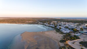 Vogelperspektive einer Küstenlandschaft mit Strand, einer Marina und einer kleinen Stadt mit Gebäuden und geparkten Fahrzeugen.