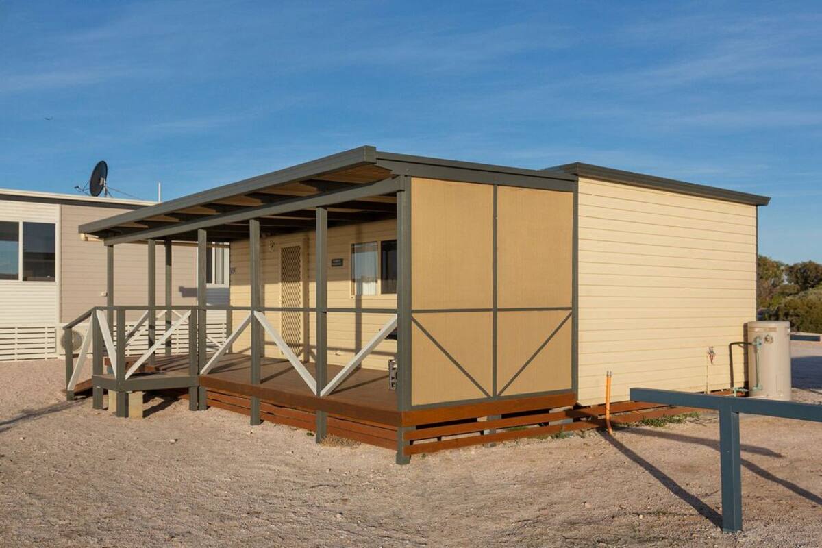 Een kleine, gelijkvloerse stacaravan met een overdekte veranda en een omheind terrein.