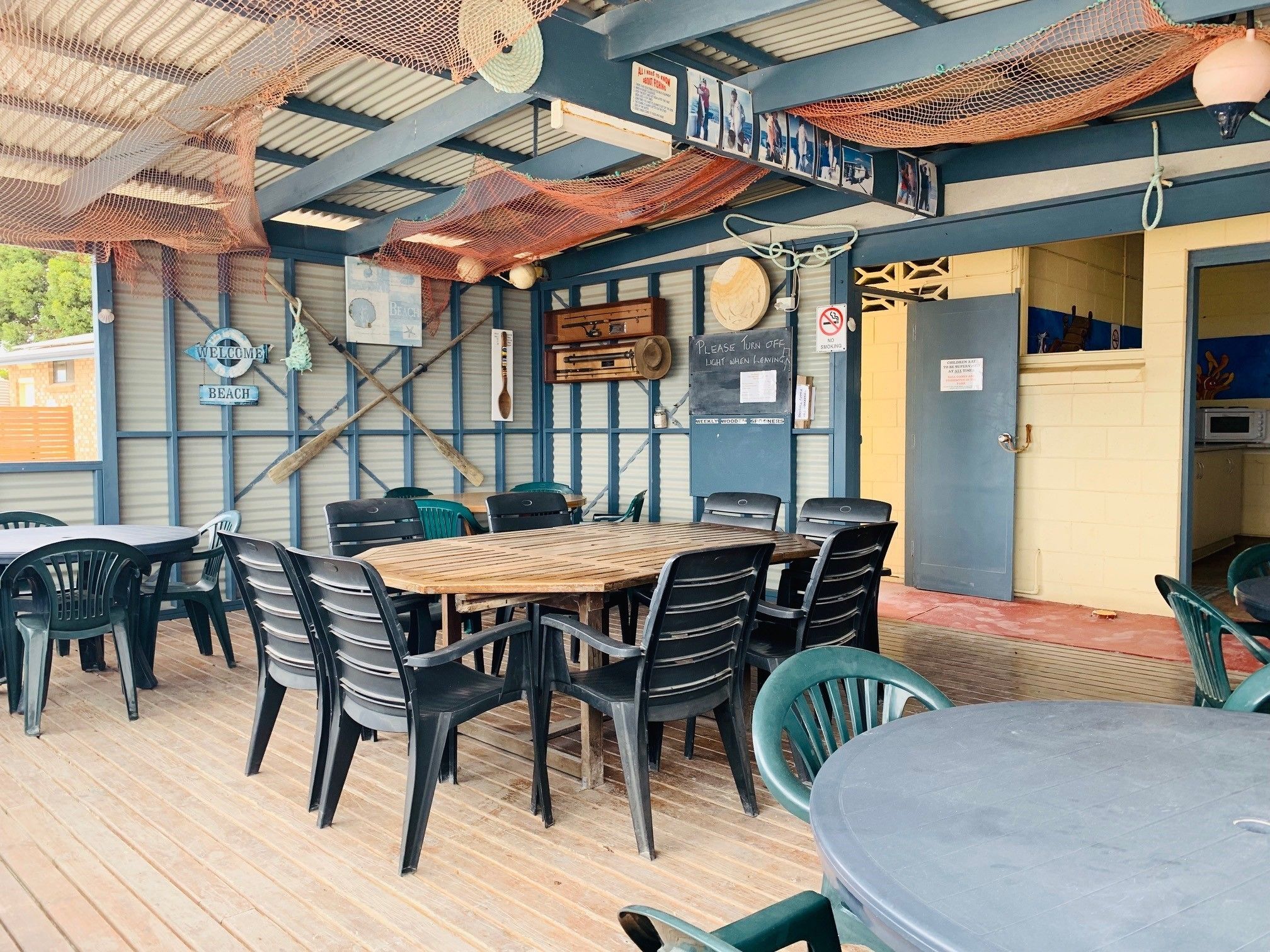 An outdoor seating area with wooden tables and plastic chairs, a wooden sign reading "Welcome Beach", and a "No Smoking" sign.