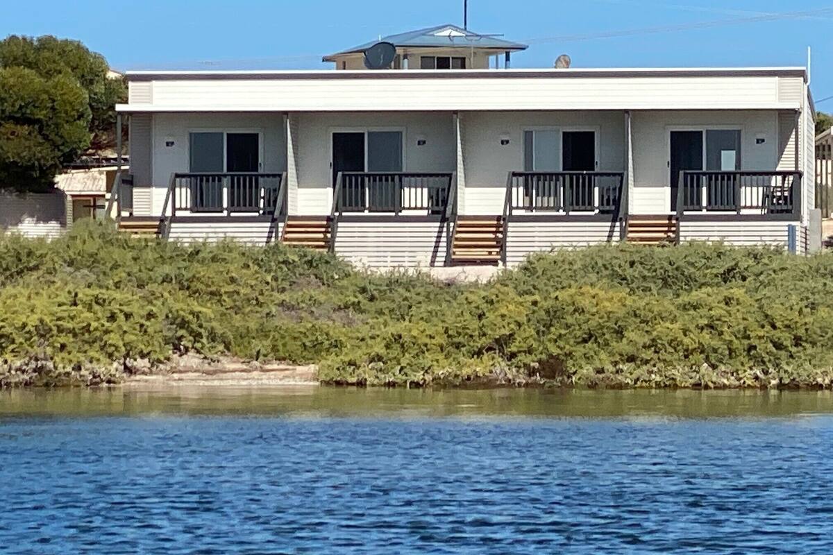 Een gebouw met twee verdiepingen, een plat dak, veel ramen en balkons. Het staat aan een waterpartij, met begroeiing op de voorgrond.