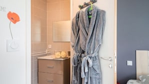 A bathroom with a towel rack holding a bathrobe, a mirror, and a sink with towels. - Chambres d'hôtes & Spa La Villa des Raspes - Adults Only (Viala-du-Tarn)