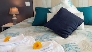 A neatly made bed with a floral bedspread, multiple pillows, and two towels with flowers on a hotel room. - Chambres d'hôtes & Spa La Villa des Raspes - Adults Only (Viala-du-Tarn)