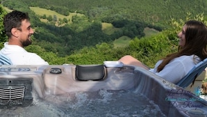 A couple relaxing in a hot tub with a scenic view of a forested valley. - Chambres d'hôtes & Spa La Villa des Raspes - Adults Only (Viala-du-Tarn)