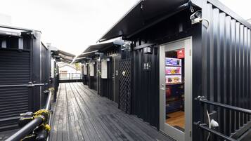 A corridor with black metal walls and a wooden deck. There is a vending machine on the right side.