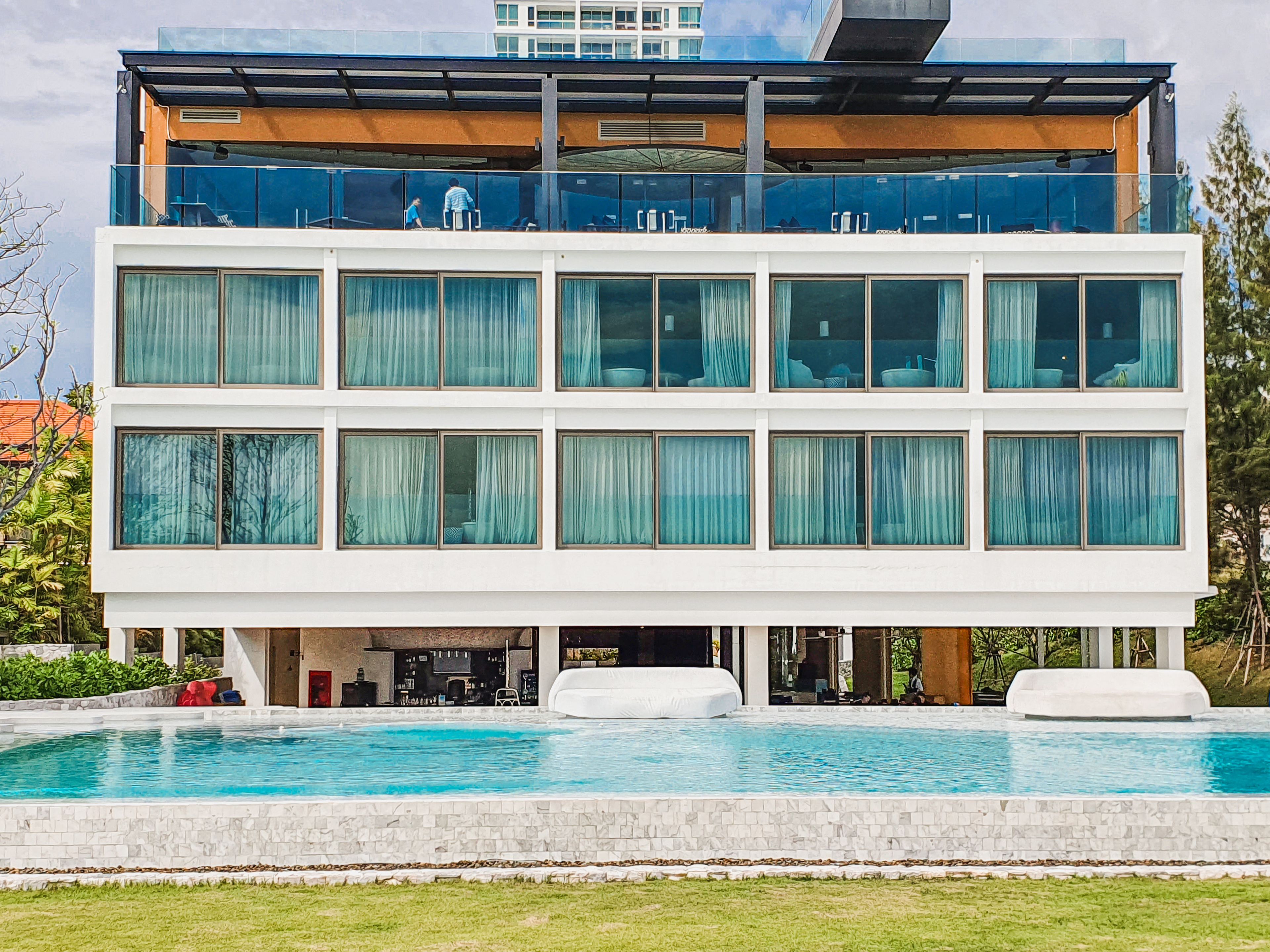 A modern multi-story building with a swimming pool in front.