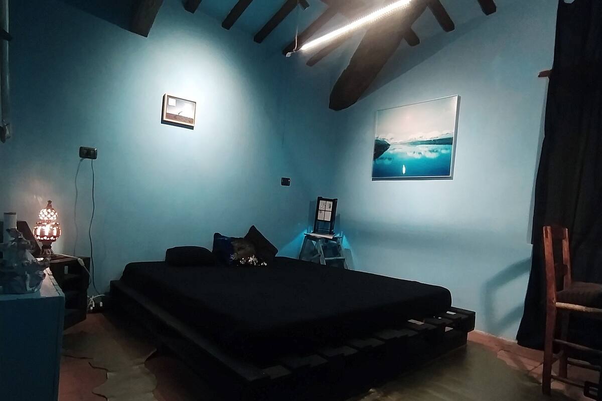 A room with a bed, a desk, a chair, a lamp, and a picture on the wall.