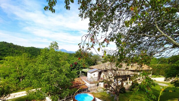 Una casa rústica con piscina, rodeada de exuberante vegetación y colinas al fondo.