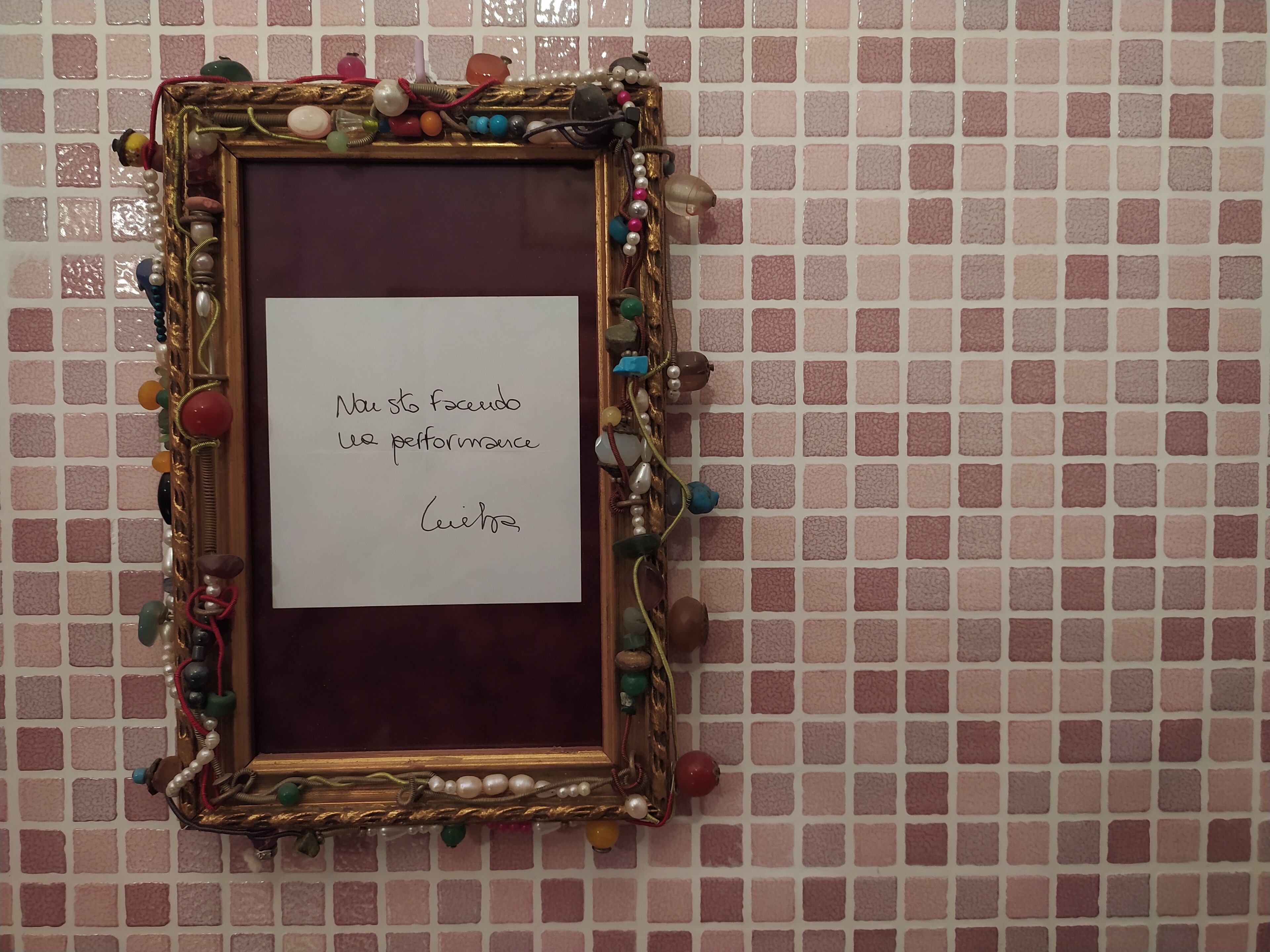 A framed note on a wall with a pink mosaic pattern.