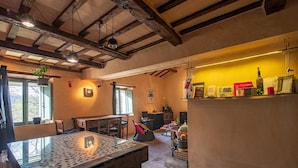 Una habitación rústica con una mesa de madera, sillas, una mesa con superficie de vidrio, un ventanal con vistas y una estantería con diversos objetos.