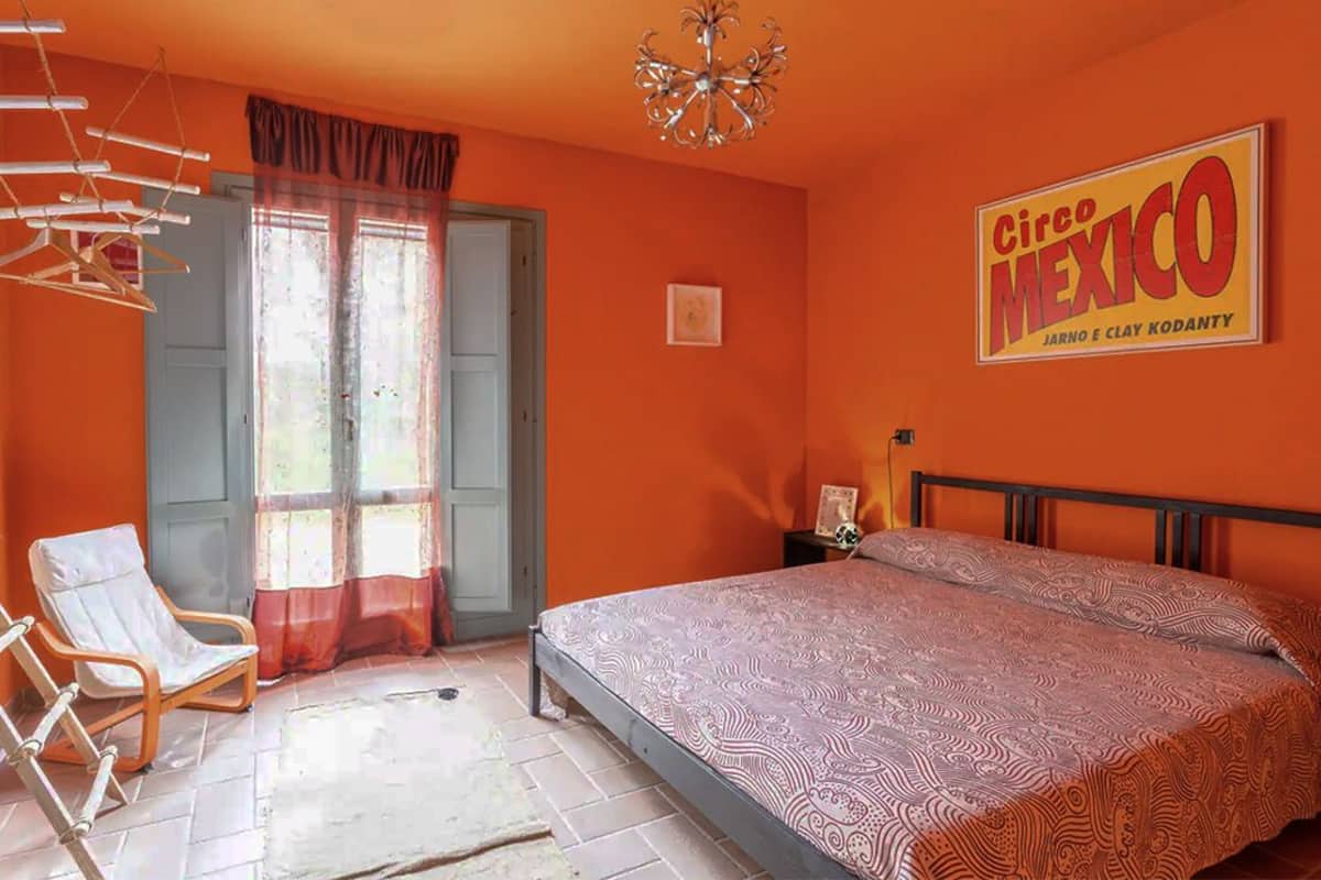 A bedroom with a bed, a chair, a chandelier, and a window with curtains.
