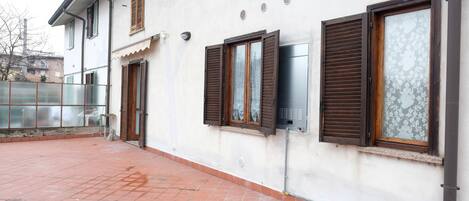 Un edificio con varias ventanas, algunas con contraventanas, y un patio con baldosas.