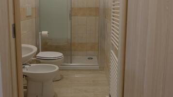 A narrow bathroom with a glass-enclosed shower, a toilet, and a sink.
