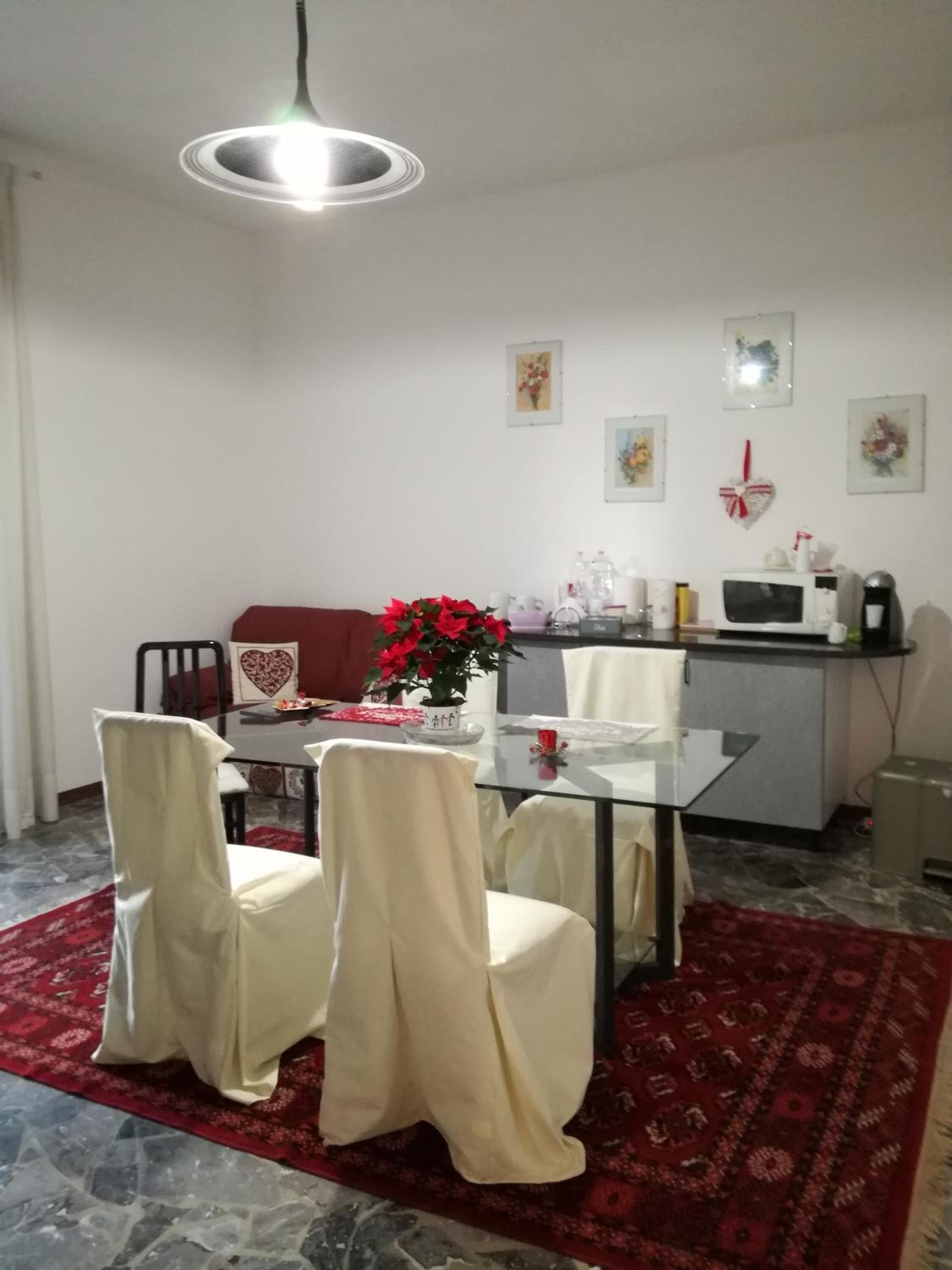 Un comedor con una mesa de vidrio, dos sillas, un tapete rojo e iluminación en el techo.