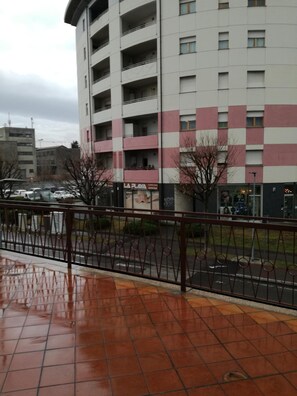 Un edificio de varios pisos con fachada a cuadros, un escaparate visible con rótulos y un camino peatonal adoquinado.
