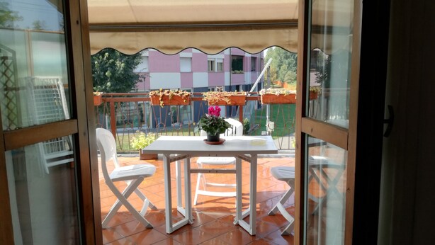 A glass door leading to an outdoor patio with a white table, two white chairs, and potted plants. - B&B Luna (Seriate)