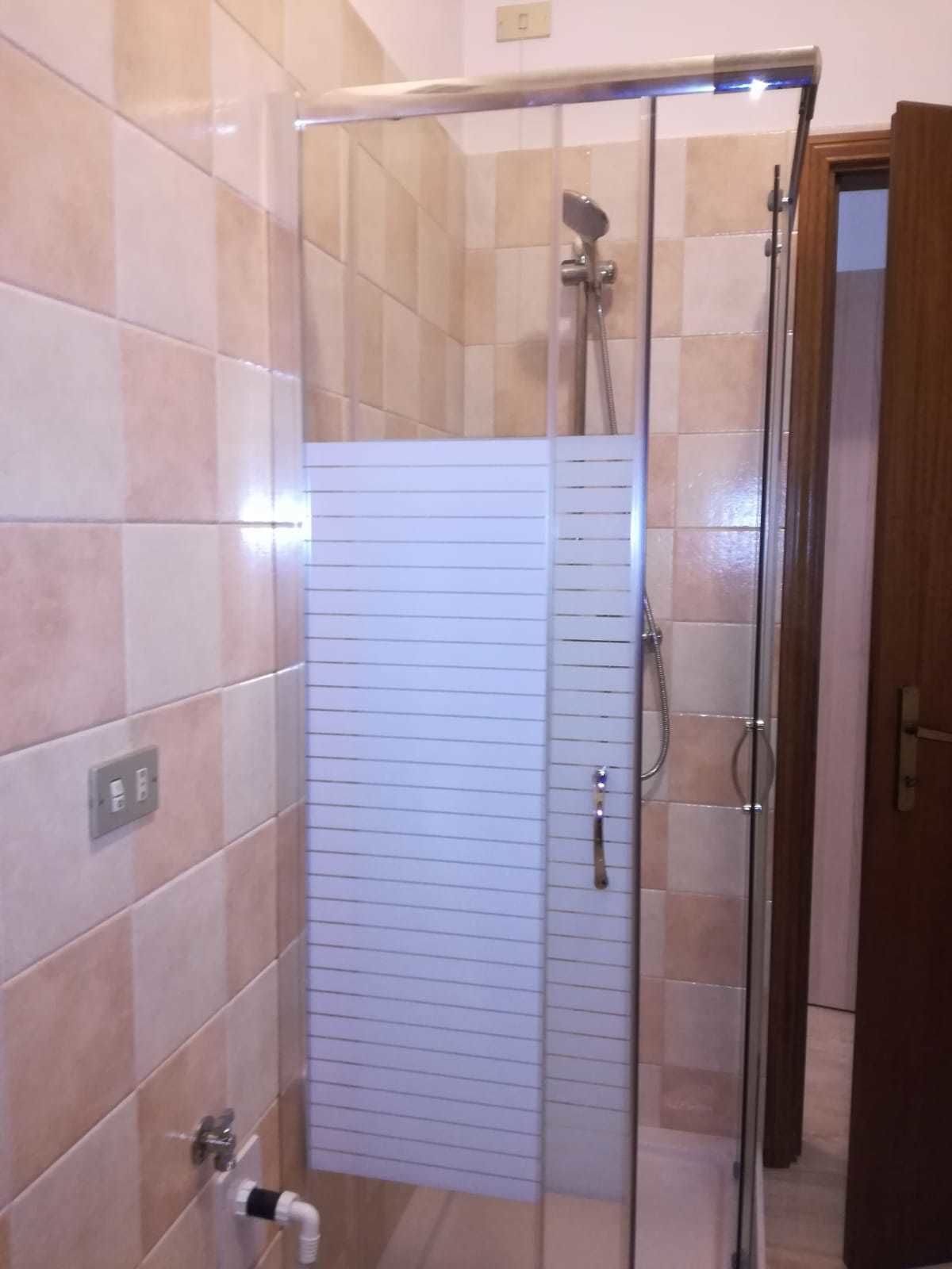 Een douche met glazen deur, betegelde wanden en een houten deur aan de rechterkant.