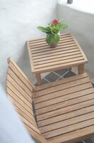 Un banco de madera y una pequeña mesa cuadrada con una planta en maceta en un balcón.