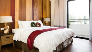 A hotel room with a large bed, wooden panel walls, two bedside tables with lamps, and a view of greenery through a large window. - Su Beautiful Homestay (Liuqiu)