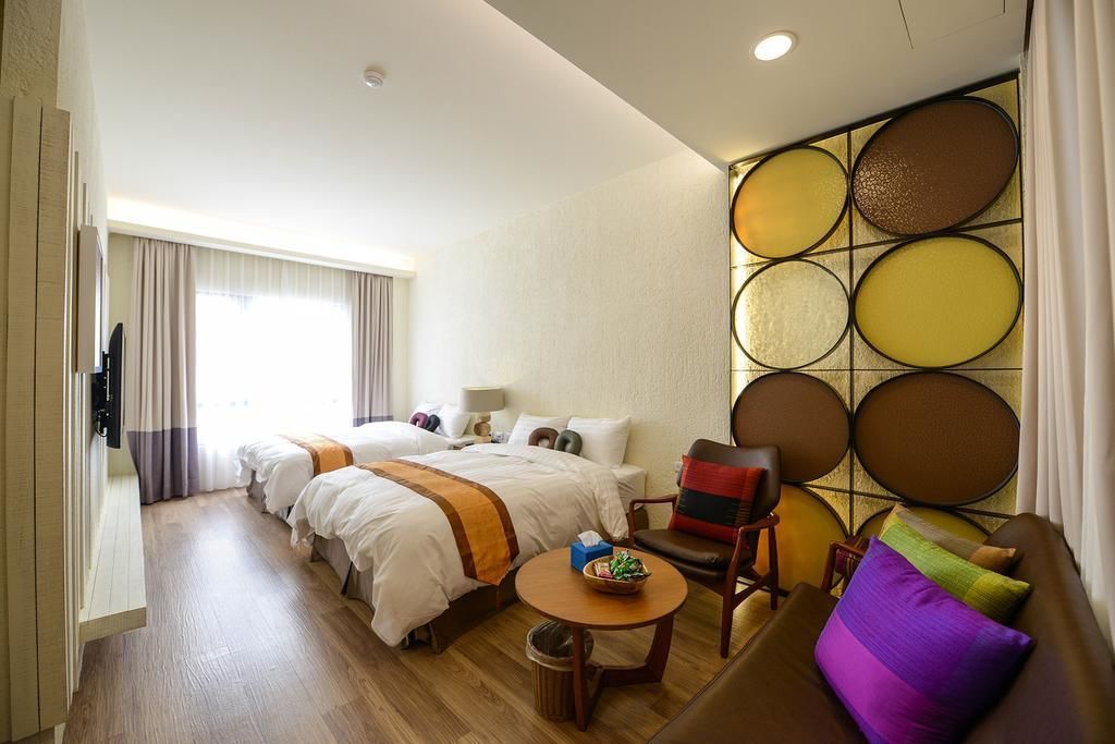 Una habitación de hotel con dos camas, un sofá, una mesita y un panel decorativo en la pared.