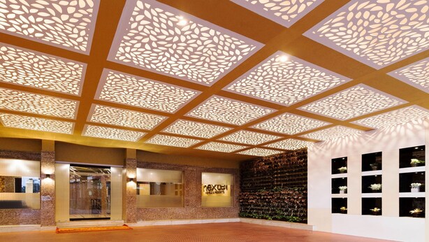 Un vestíbulo de hotel con techo estampado, una zona de recepción y una pared con plantas en macetas.