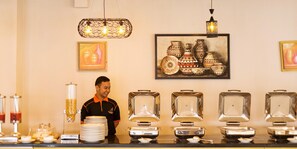 A buffet setup with multiple serving stations, a person standing behind the counter, and decorative wall art.