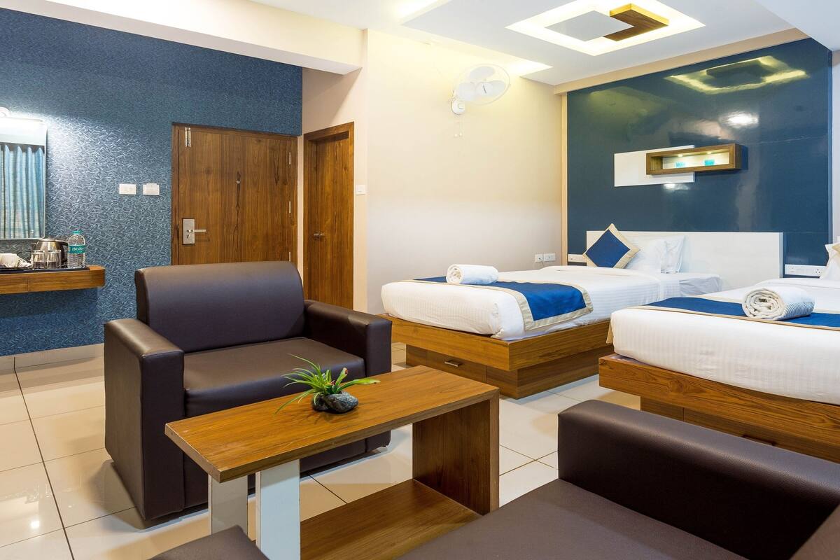 A hotel room with two beds, a sofa, a wooden table, and a small plant.