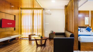 Una habitación de hotel moderna con piso de madera, una televisión de pantalla plana, un sofá, una cama y una mesita.