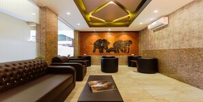 A lobby with a brown leather sofa, black ottomans, a marble floor, and a wall with an elephant mural.