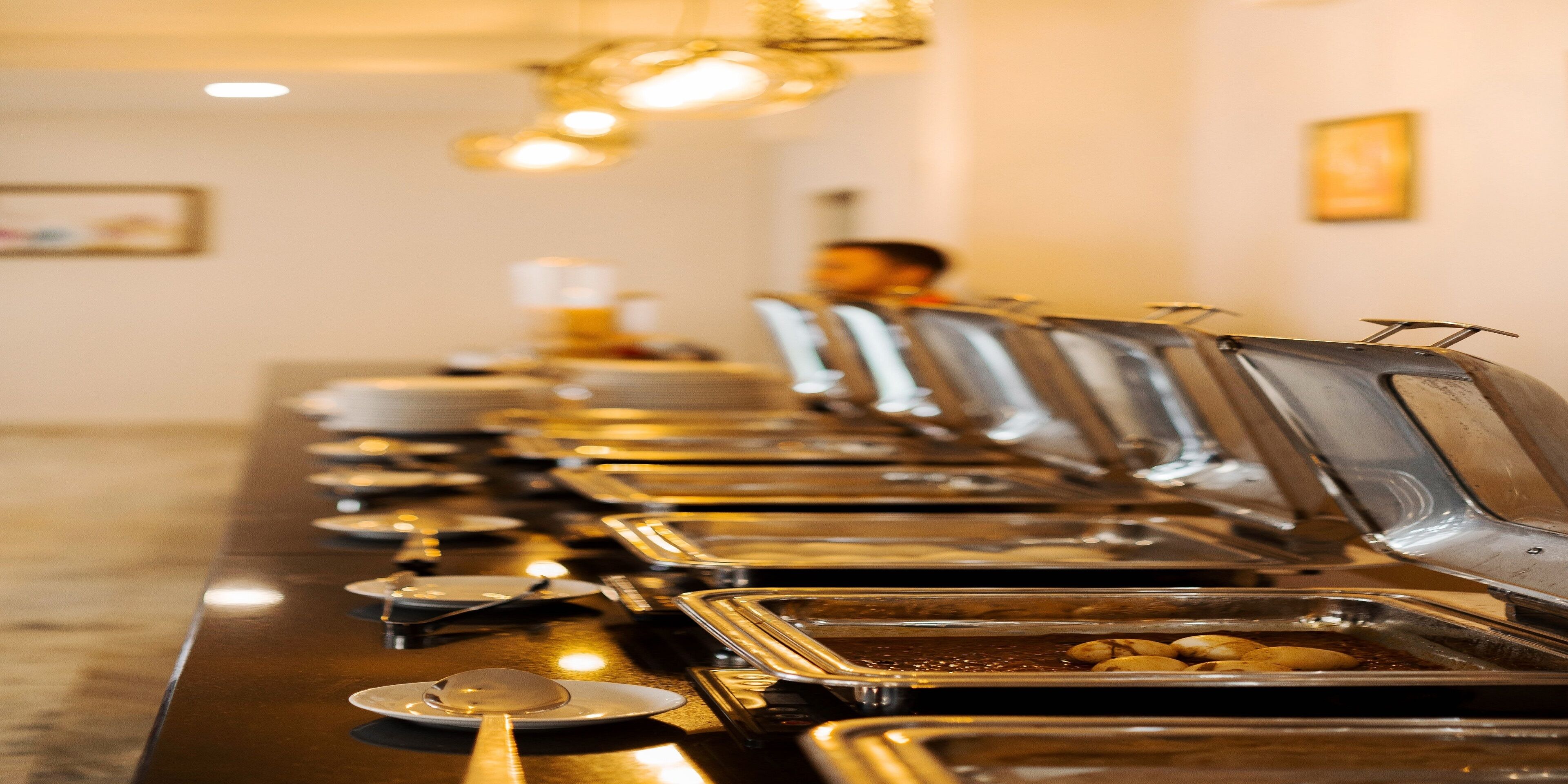 A buffet line with multiple food stations, each with a metal tray and a spoon.