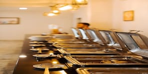 Una mesa de buffet con varias estaciones de comida, cada una con una bandeja metálica y una cuchara.