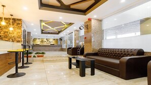 Un hall de hotel con mostrador de recepción, un sofá, una mesa de centro y una zona de bar con taburetes.