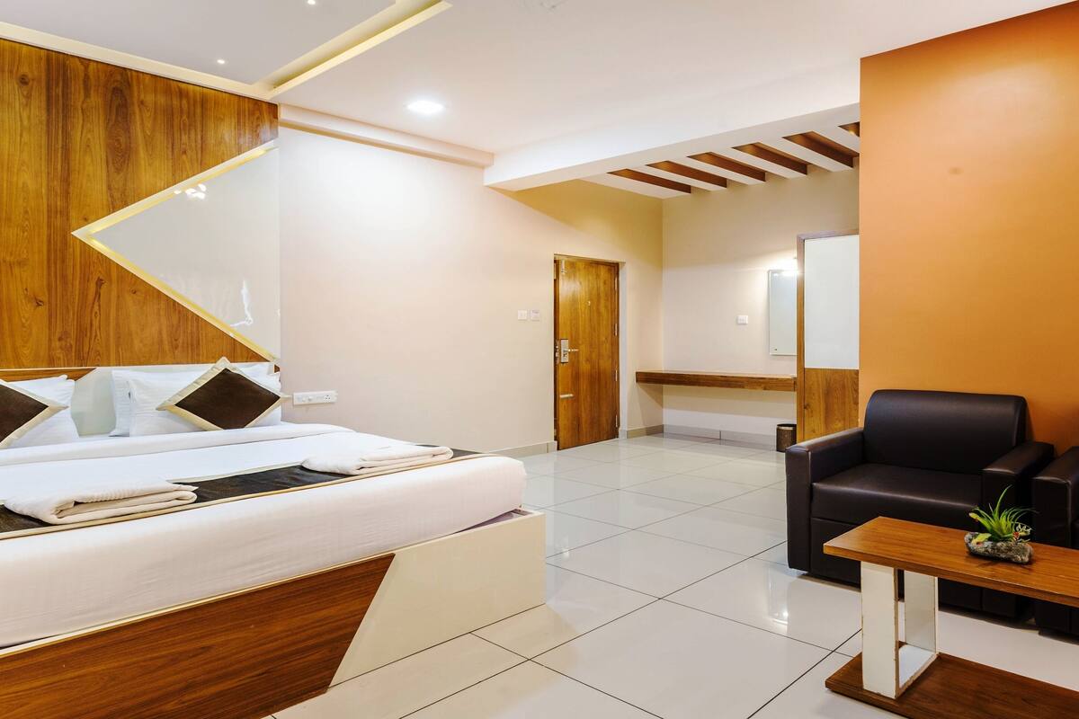A modern hotel room with a bed, a black leather sofa, a wooden coffee table, and a small plant.
