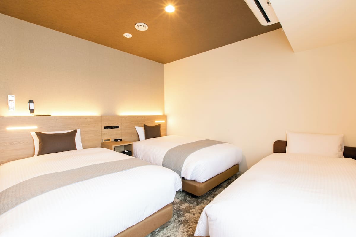 A hotel room with two beds, a wooden headboard, a nightstand, and a wall-mounted light fixture.