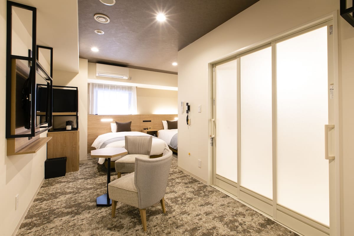 A hotel room with a bed, a chair, a desk, a TV, and a wardrobe.
