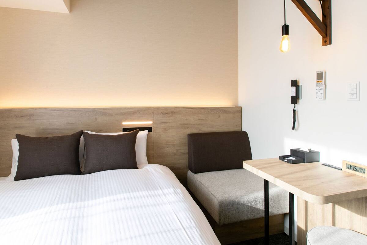 A hotel room with a bed, bedside tables, a desk, and a wall-mounted phone.