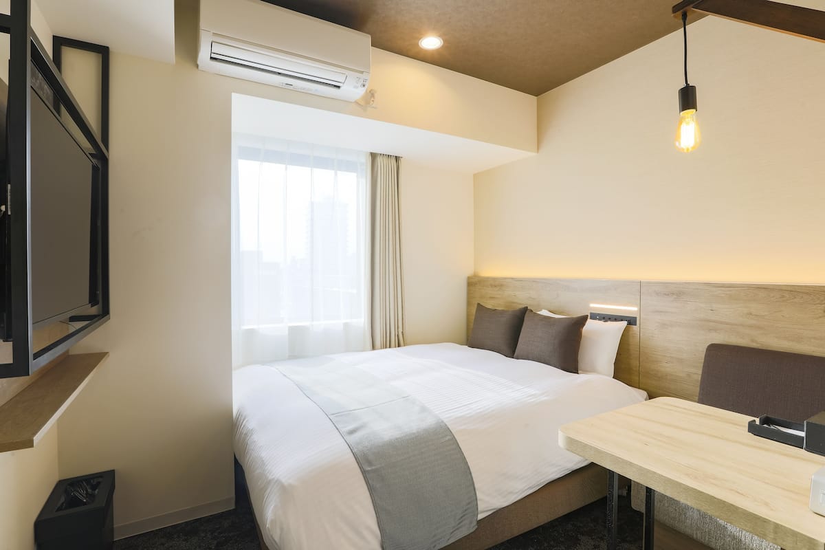 A hotel room with a bed, bedside table, and a TV mounted on the wall.