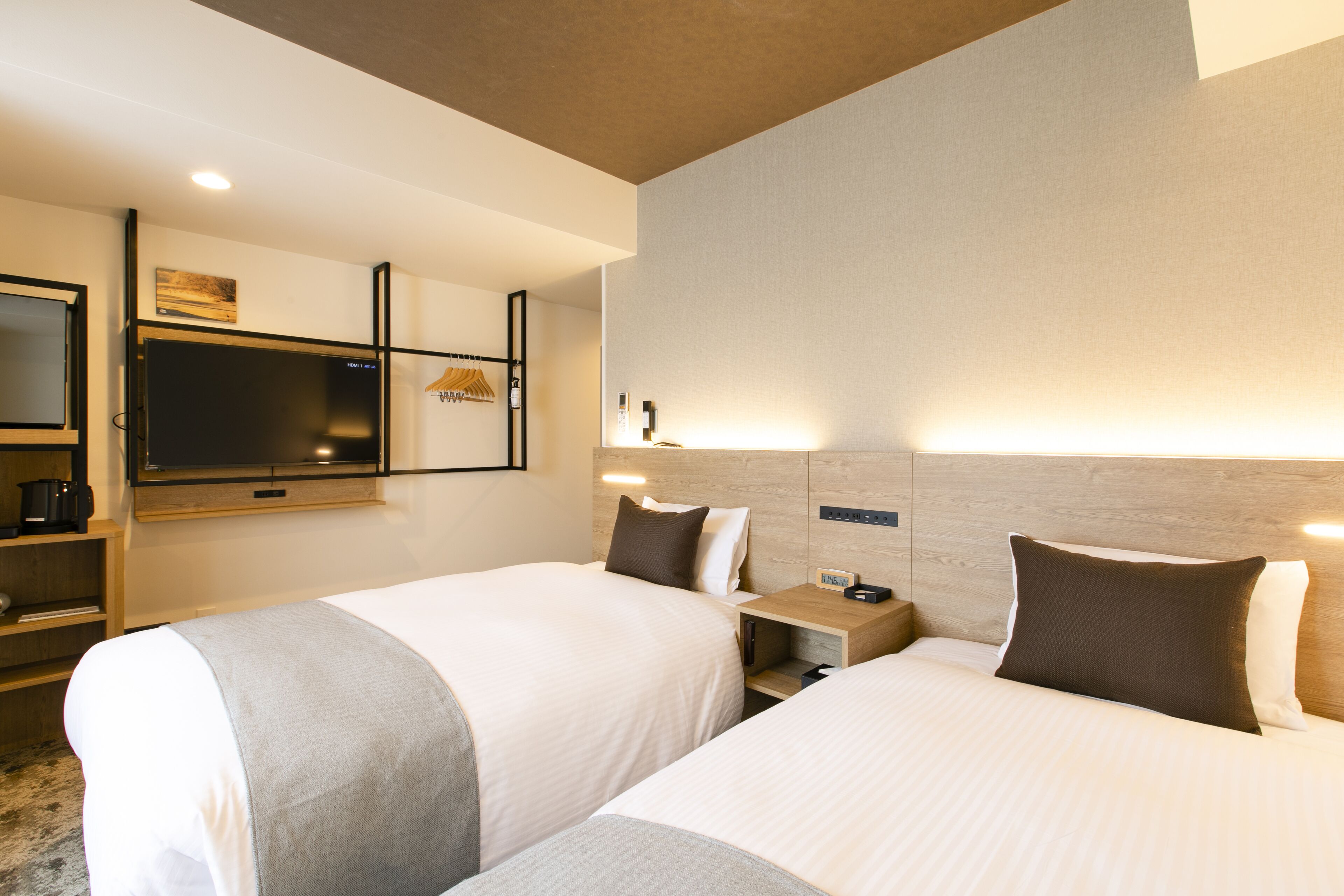 Une chambre d’hôtel avec deux lits, une télévision, une table de chevet et une étagère fixée au mur.