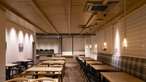 Un restaurant moderne avec des tables et des chaises en bois, un comptoir central et des luminaires suspendus.