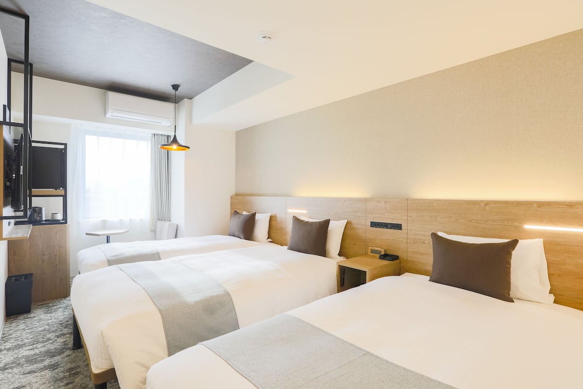 A hotel room with two beds, a desk, a chair, a TV, and a window with curtains.