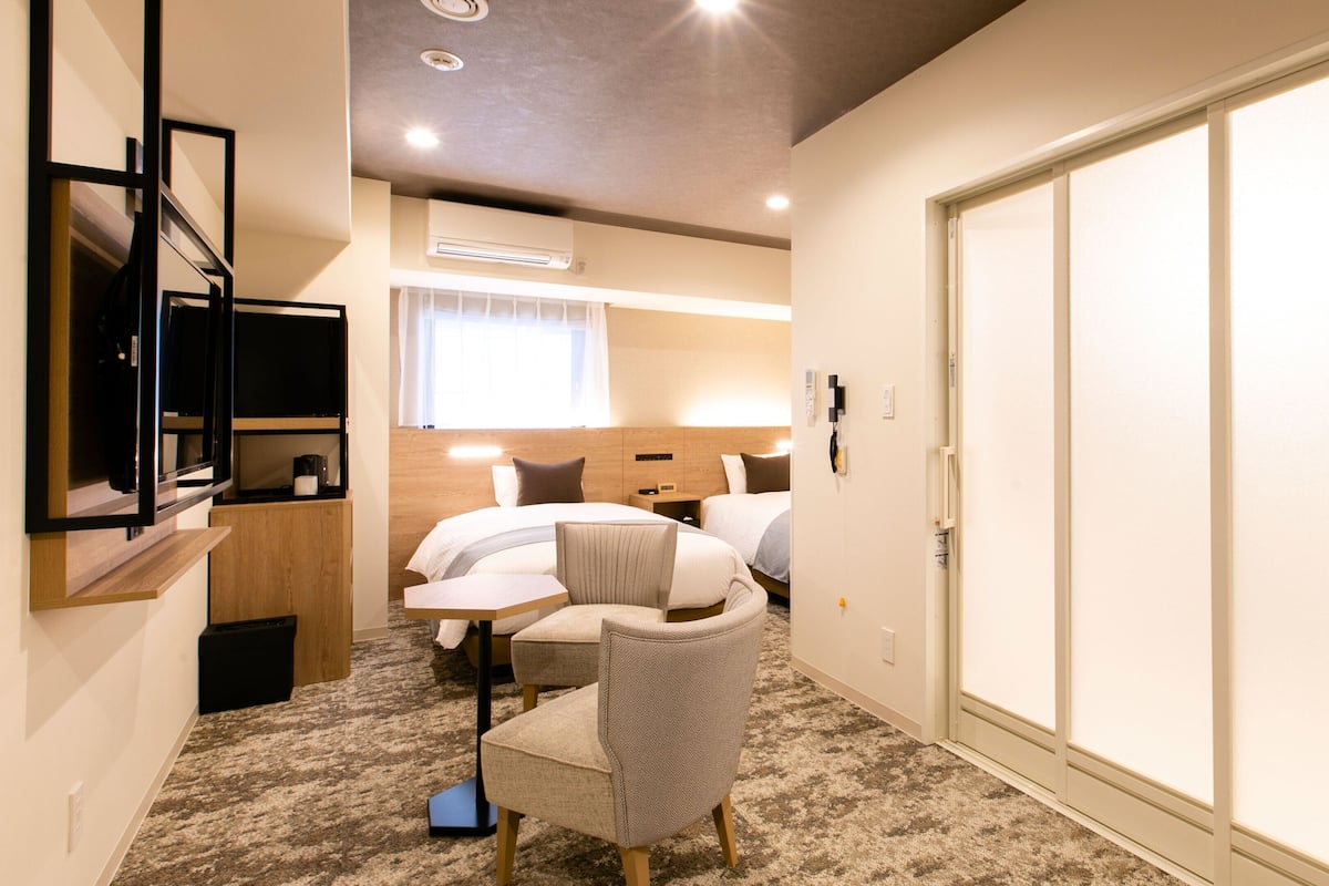 A hotel room with a bed, bedside tables, a chair, a desk, a flat-screen TV, and a wardrobe.