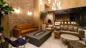 Un espace de détente moderne avec un mur en briques, un plafond en bois et un mobilier contemporain comprenant des canapés, une table basse et un coin salon avec une petite table et des chaises.