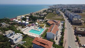 An aerial view of a coastal area with a swimming pool, buildings, and a road.