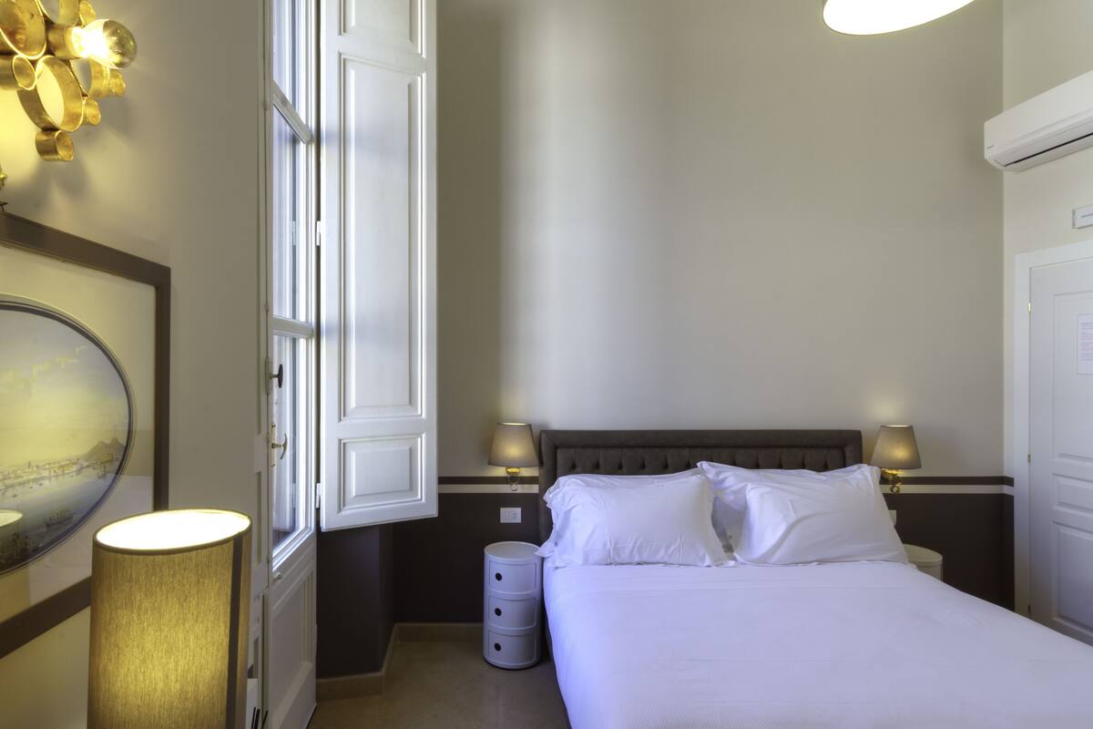Une chambre d’hôtel avec un lit, des lampes de chevet, un miroir et une fenêtre avec des rideaux.