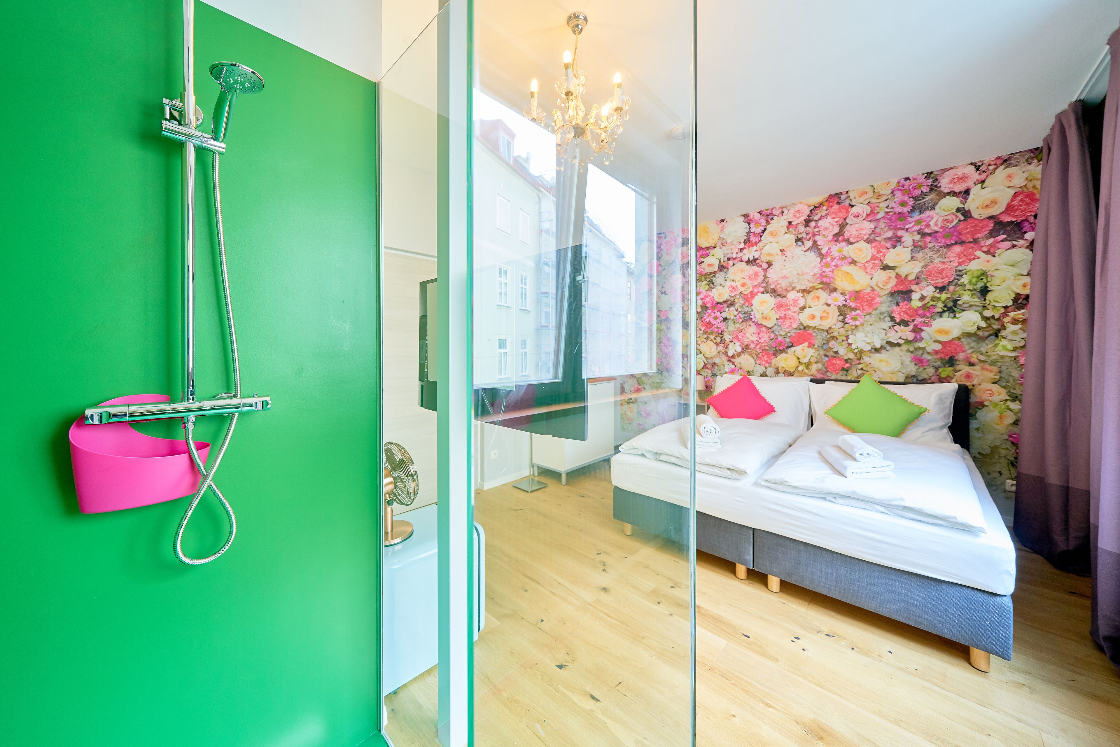 Una camera d'albergo moderna con box doccia in vetro, un letto con carta da parati a motivi floreali e vista sulla città.