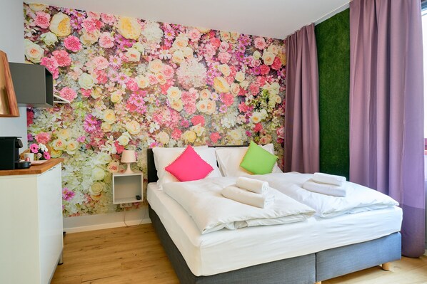 A bedroom with a floral wallpaper, a bed with white linens, two pillows, a bedside table with a lamp, and a green accent wall. - Leuhusen Center Apartments Vienna (Vienna)